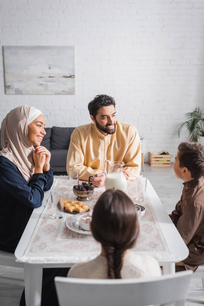 Famille musulmane souriante parlant près de la nourriture pendant le ramadan à la maison  - Photo, image