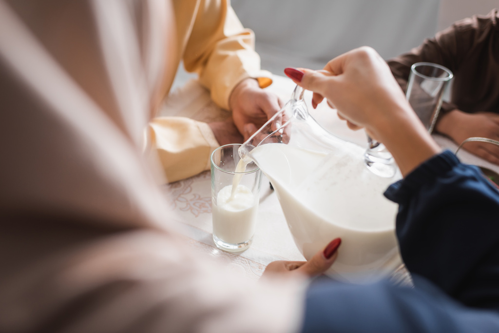 Mujer árabe vertiendo leche durante el suhur con la familia en la mañana en casa  - Foto, Imagen