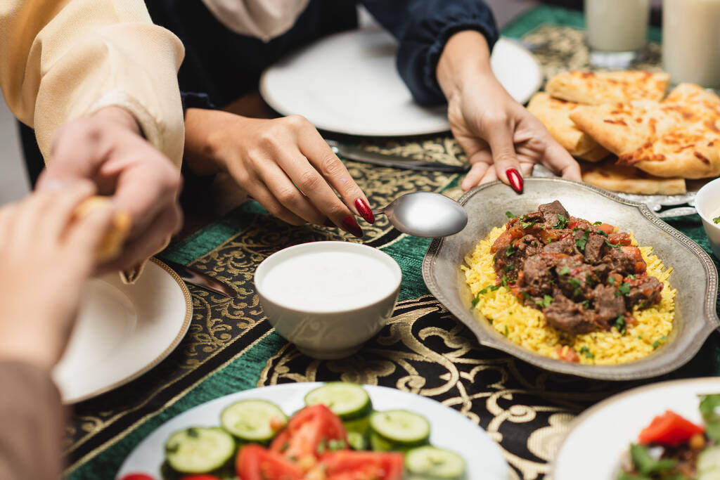 Vista recortada de la mujer musulmana poniendo pilaf en la mesa durante la cena de ramadán  - Foto, imagen