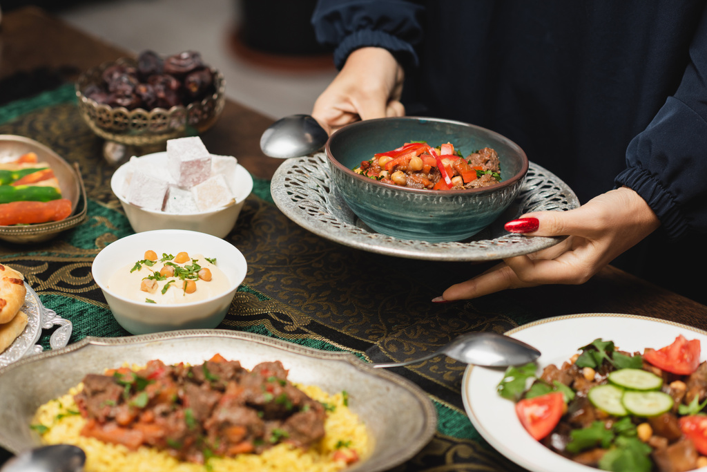 Καλλιεργημένη θέα μουσουλμάνου γυναίκα κρατώντας νόστιμο γεύμα κοντά στο τραπέζι κατά τη διάρκεια του δείπνου ραμαντάν  - Φωτογραφία, εικόνα