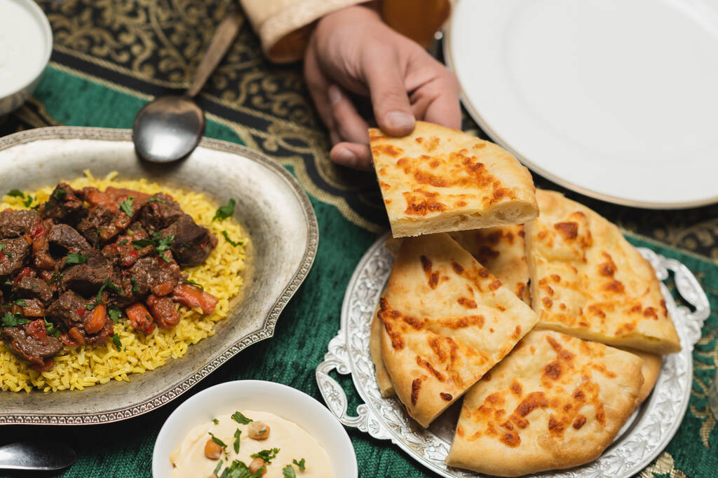 Cropped view of muslim man holding pita bread near pilaf on table at home  - Photo, Image