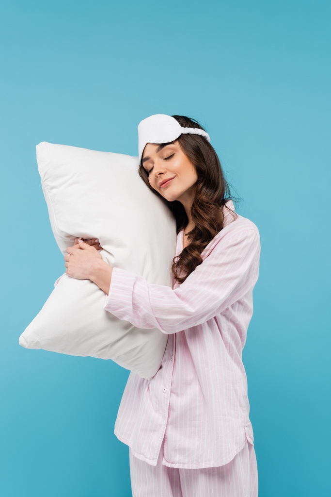 young woman in pajamas and night mask sleeping on white pillow isolated on blue  - Foto, Imagen
