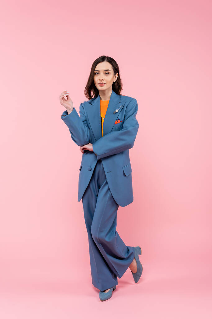 full length of young brunette woman in blue pantsuit standing on pink  - Foto, Imagen