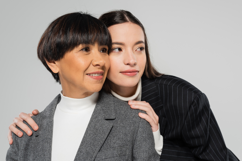 positive asian mother and daughter in white turtlenecks and blazers looking away isolated on grey - Fotoğraf, Görsel