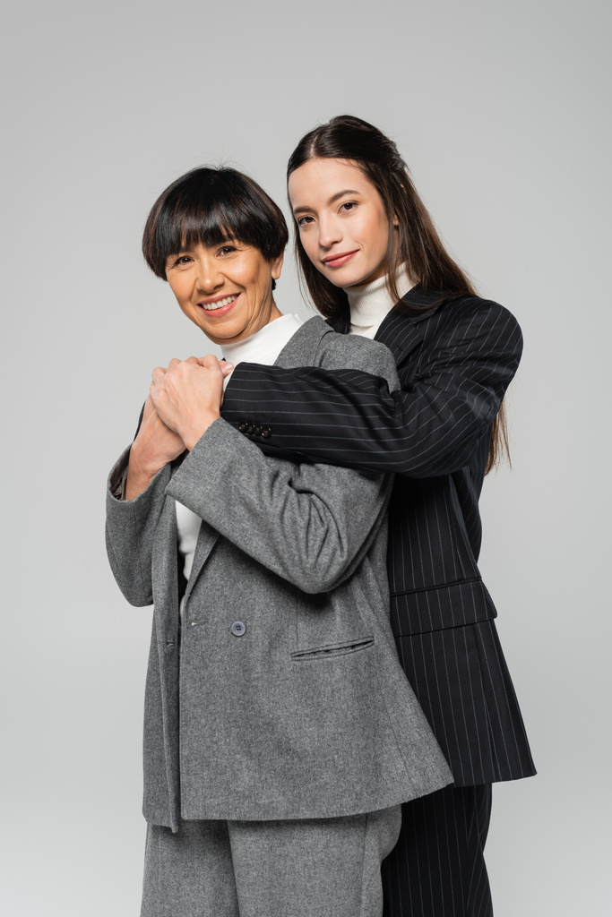 cheerful asian mother and daughter in stylish blazers looking at camera isolated on grey - Photo, Image