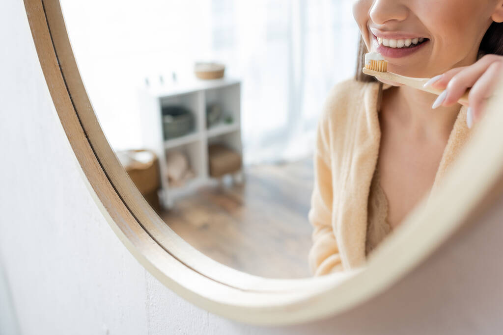cropped view of young and cheerful woman brushing teeth near mirror in bathroom - Photo, Image