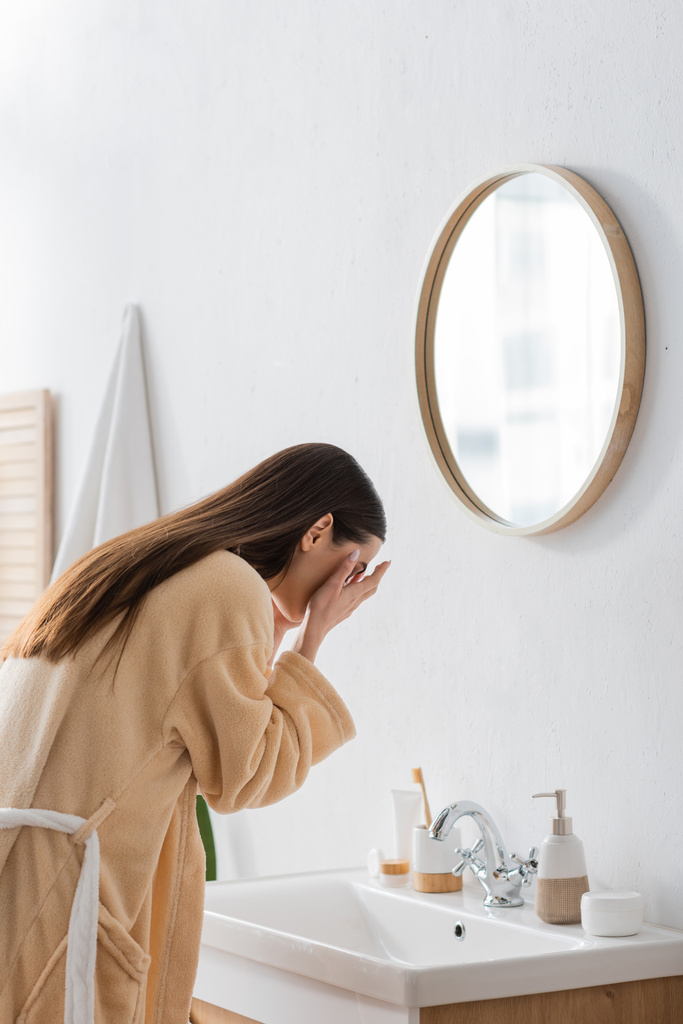 jeune femme brune avec des cheveux longs lavage visage dans la salle de bain  - Photo, image