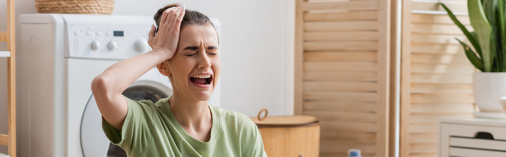 smutna kobieta dotykająca głowy i płacząca w pralni, baner  - Zdjęcie, obraz