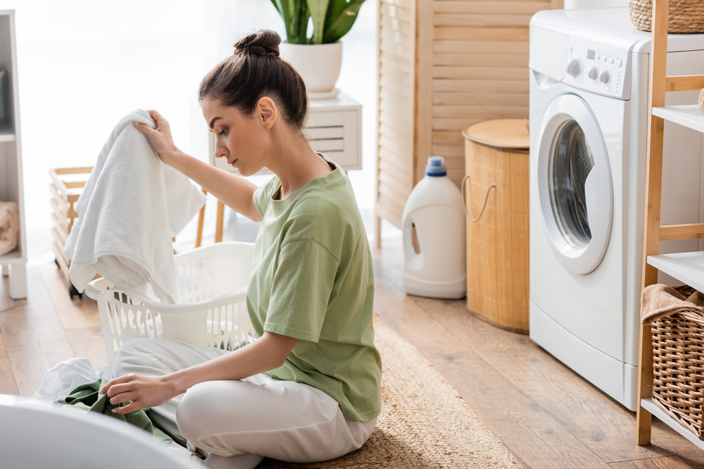 вид збоку брюнетка жінка сортування одягу в пральні
  - Фото, зображення