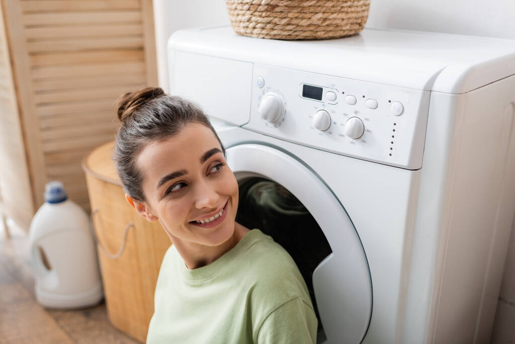 Усміхнена жінка дивиться на пральну машину вдома
 - Фото, зображення
