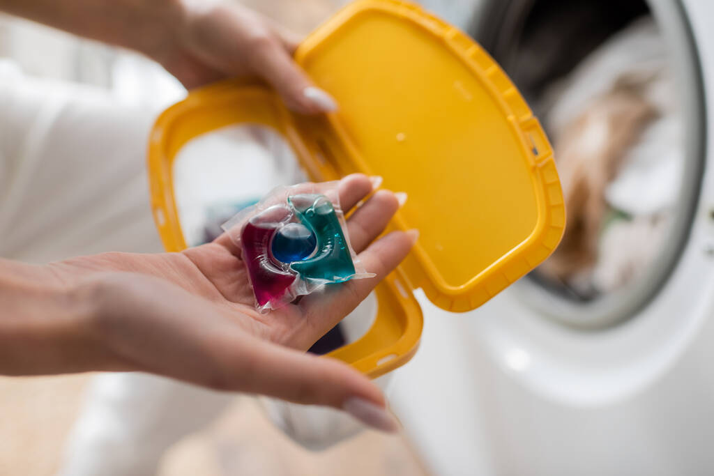 Widok kobiety trzymającej kapsułkę myjącą i niewyraźne pudełko w pralni  - Zdjęcie, obraz