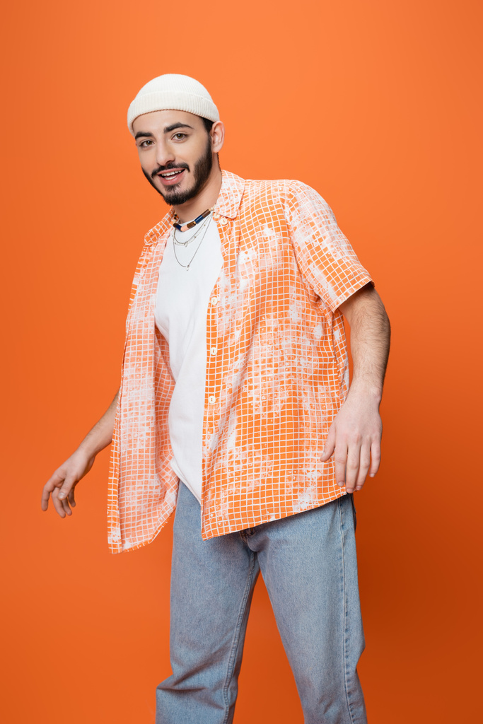 オレンジに隔離されながらカメラで微笑む流行のカジュアルな服装の若い髭男 - 写真・画像