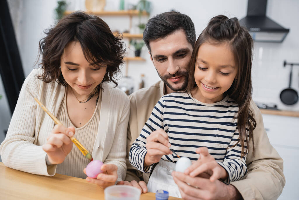 glückliche Familie lächelt beim Färben von Ostereiern in der Küche  - Foto, Bild