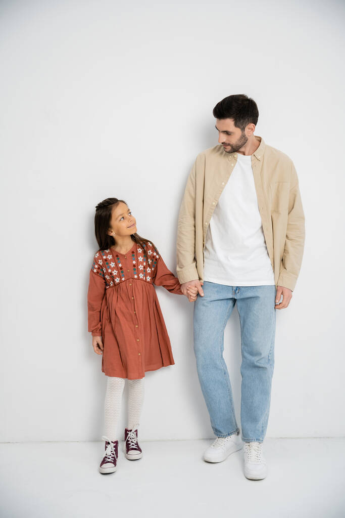 Smiling man holding hand of preteen daughter on white background  - Fotó, kép