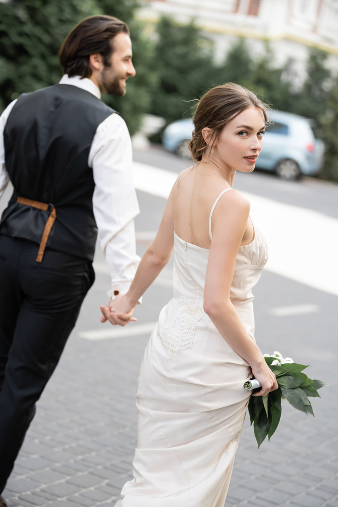 наречений тримає руку розкішної нареченої у весільній сукні з букетом квітів
  - Фото, зображення