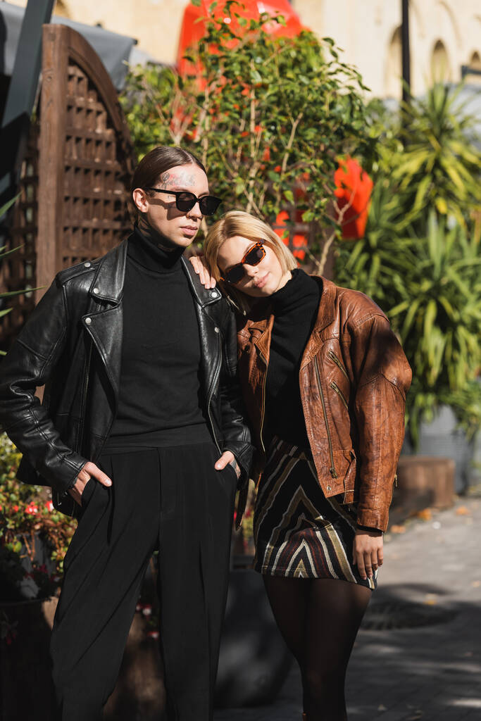 blonde woman in sunglasses leaning on shoulder of stylish man posing with hands in pockets  - Foto, Imagem