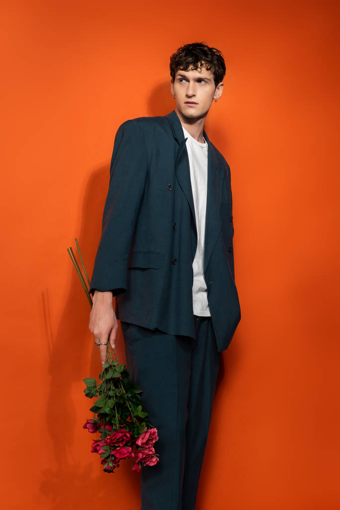 Stylish model in blue suit holding roses on orange background  - Fotó, kép