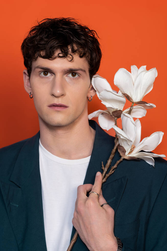 Portrait of stylish curly man holding magnolia branch isolated on orange - Photo, image