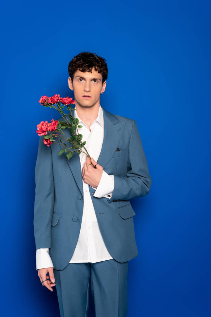 Curly man in suit holding red flowers on blue background  - Foto, immagini