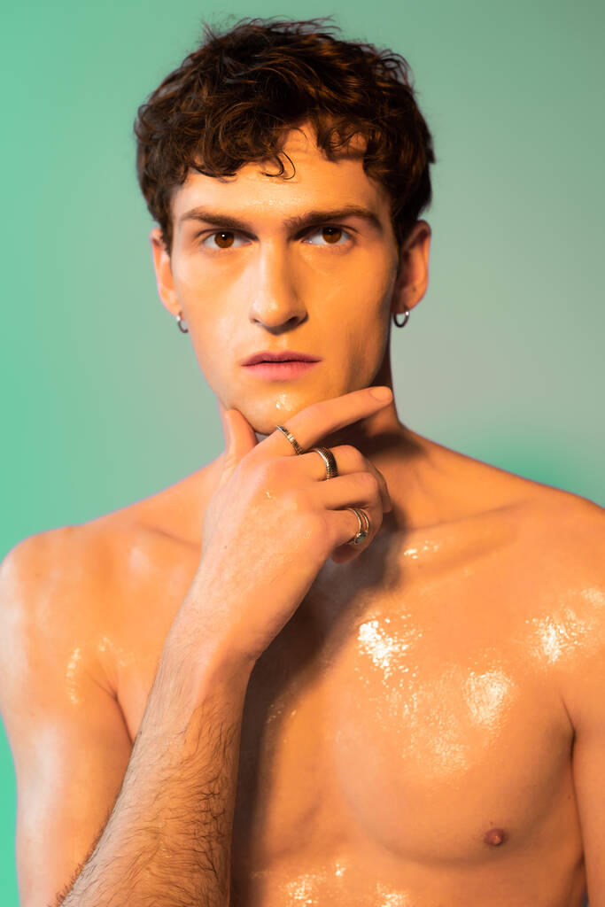 Portrait of shirtless man with oil on skin looking at camera on green background  - Photo, image