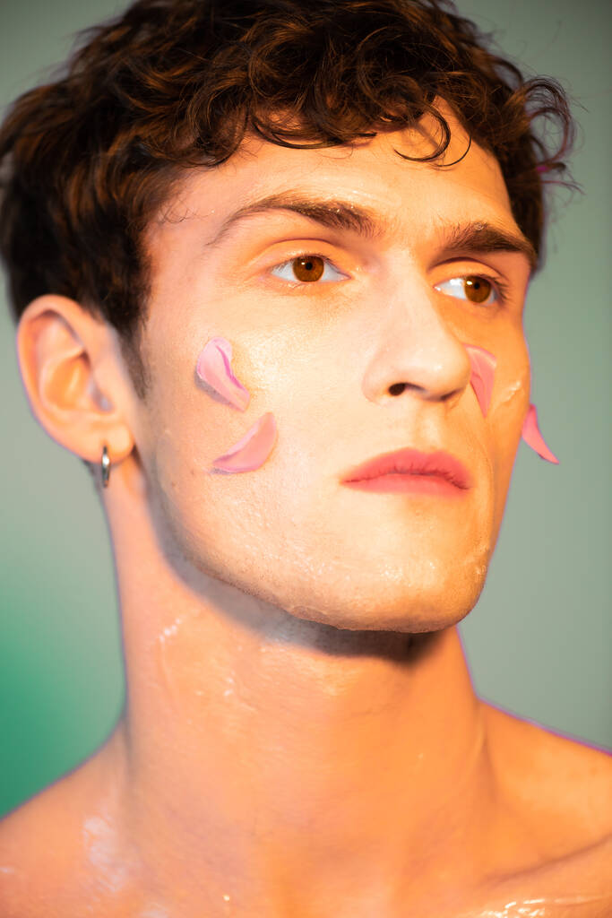 Портрет молодого чоловіка з пелюстками на обличчі, який дивиться на барвистий фон
  - Фото, зображення