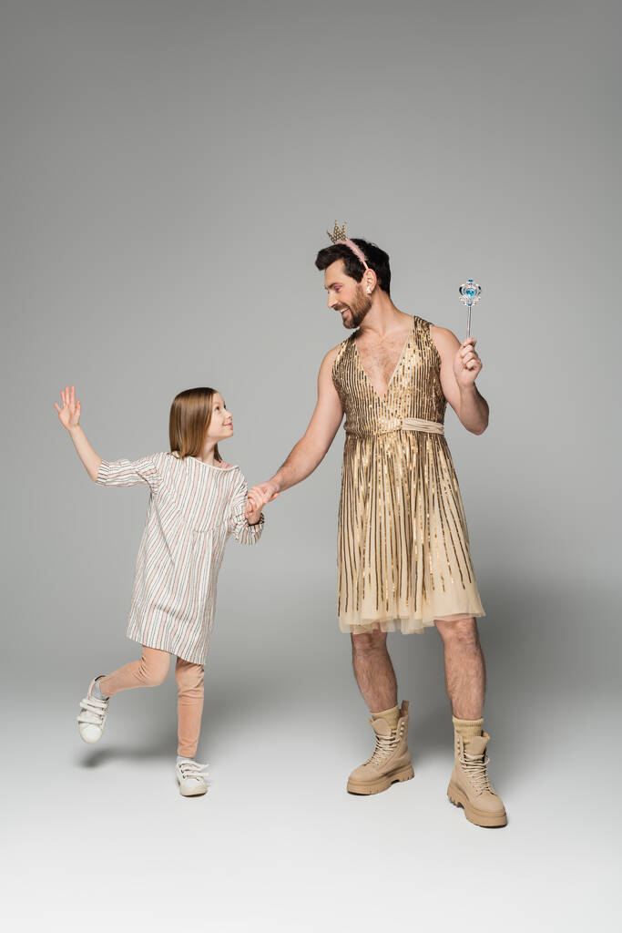 ドレスの女の子の完全な長さで手に手でお父さんでドレスとおもちゃの杖でグレー  - 写真・画像