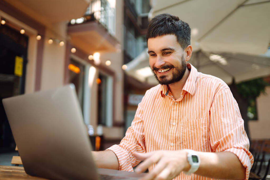 Bilgisayarı ve telefonu olan genç bir adam bir kafede oturuyor ve çalışıyor. İş, blog yazma, serbest çalışma, eğitim kavramı. - Fotoğraf, Görsel