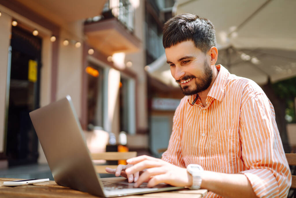 Mladý muž s laptopem a telefonem sedí v kavárně a pracuje. Byznys, blogování, volný čas, koncepce vzdělávání. - Fotografie, Obrázek