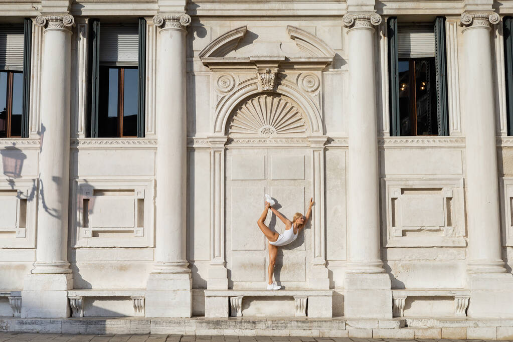 ヴェネツィアの建物の近くにストレッチボディスーツやスニーカーのスポーツ女性の側面図  - 写真・画像