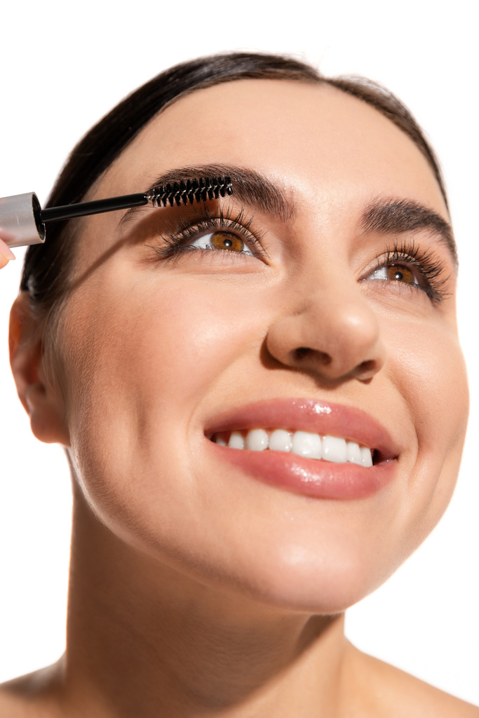 close up of cheerful woman applying mascara while looking up isolated on white  - Φωτογραφία, εικόνα