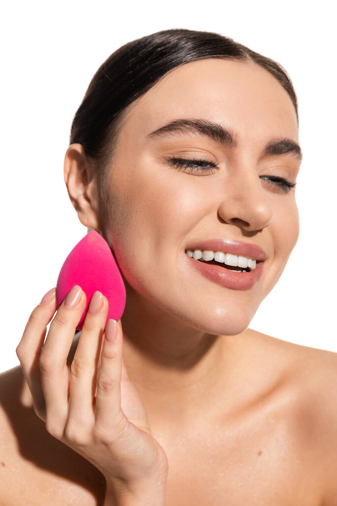 heureuse jeune femme appliquant fond de teint de maquillage avec éponge beauté rose isolé sur blanc  - Photo, image