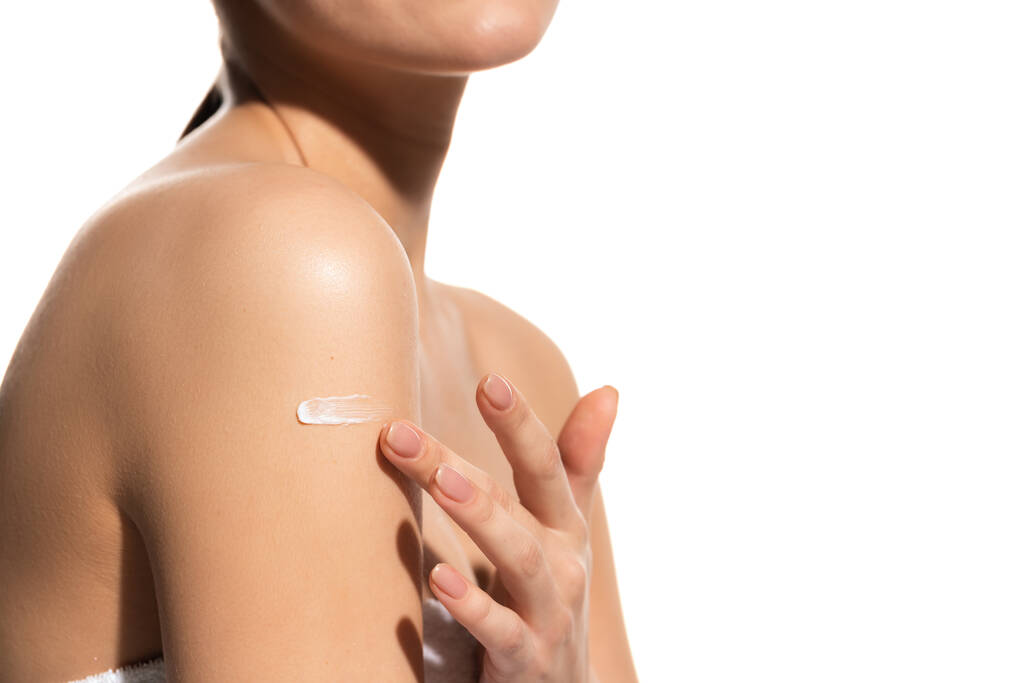 vista recortada de la mujer joven aplicación de loción en el cuerpo aislado en blanco  - Foto, imagen