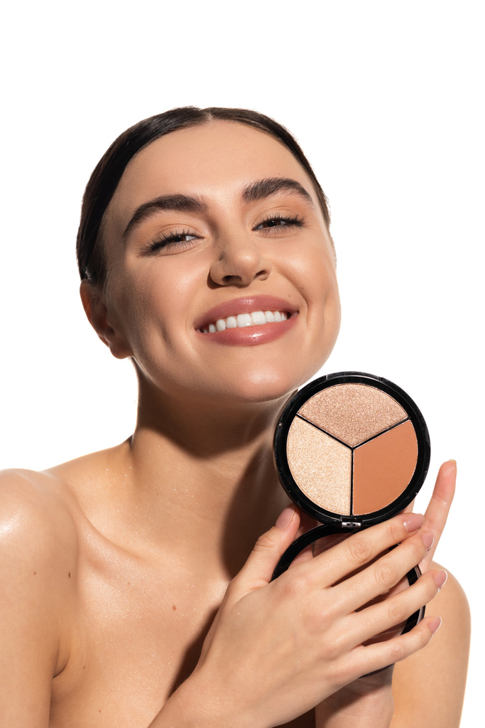 positive young woman with bare shoulders holding bronzer and highlighter palette isolated on white  - Foto, immagini