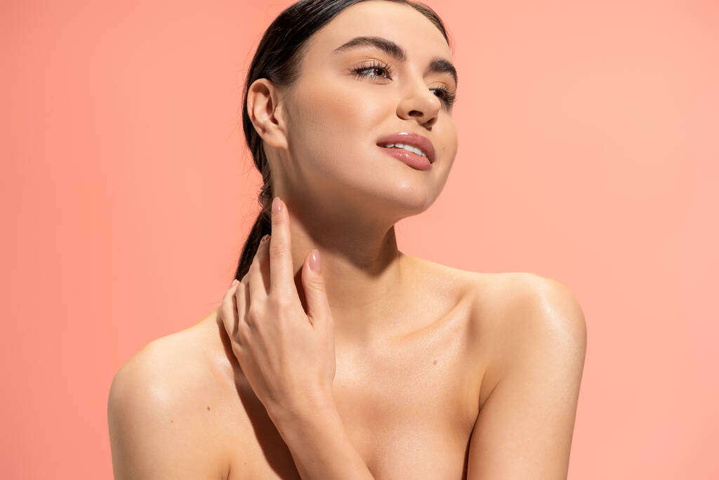 довольная женщина с голыми плечами и безупречный макияж касаясь мягкой кожи изолированы на розовый  - Фото, изображение