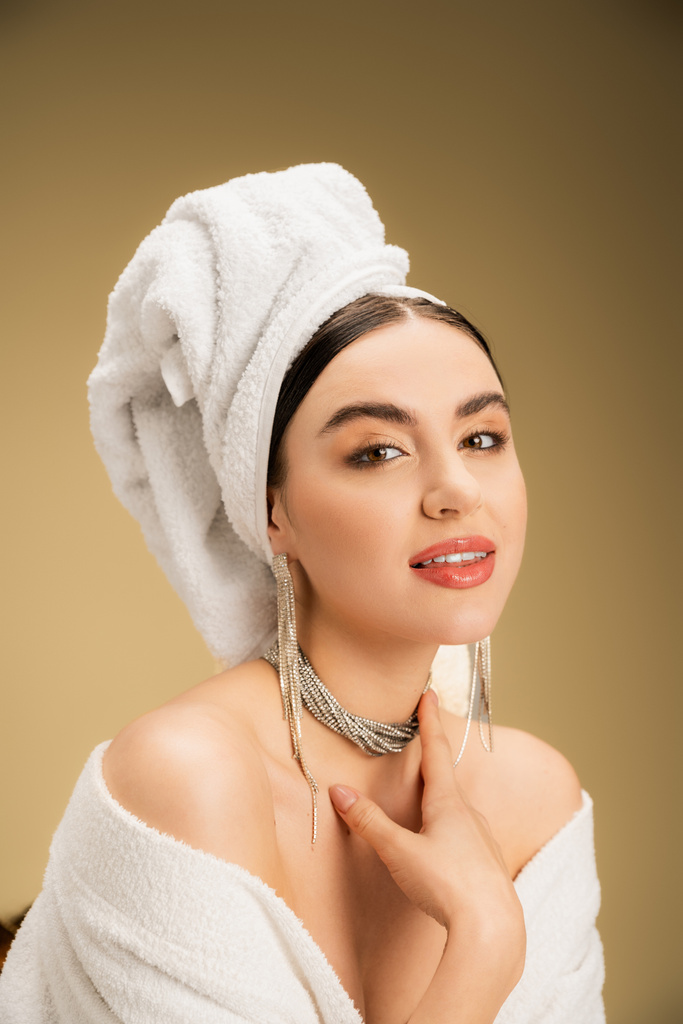 cheerful woman with makeup and towel on head looking at camera on beige background  - Fotografie, Obrázek