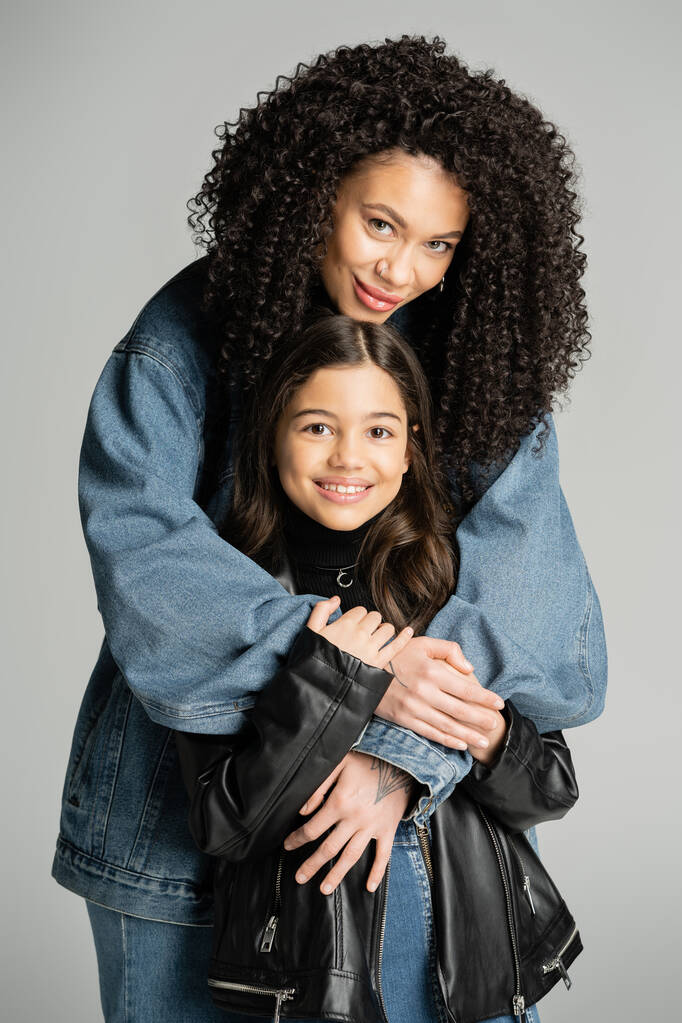 Smiling woman in denim jacket hugging daughter isolated on grey  - Foto, afbeelding