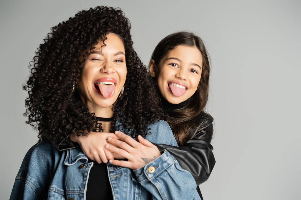 Lockige Frau und Tochter strecken die Zungen vereinzelt auf grau - Foto, Bild