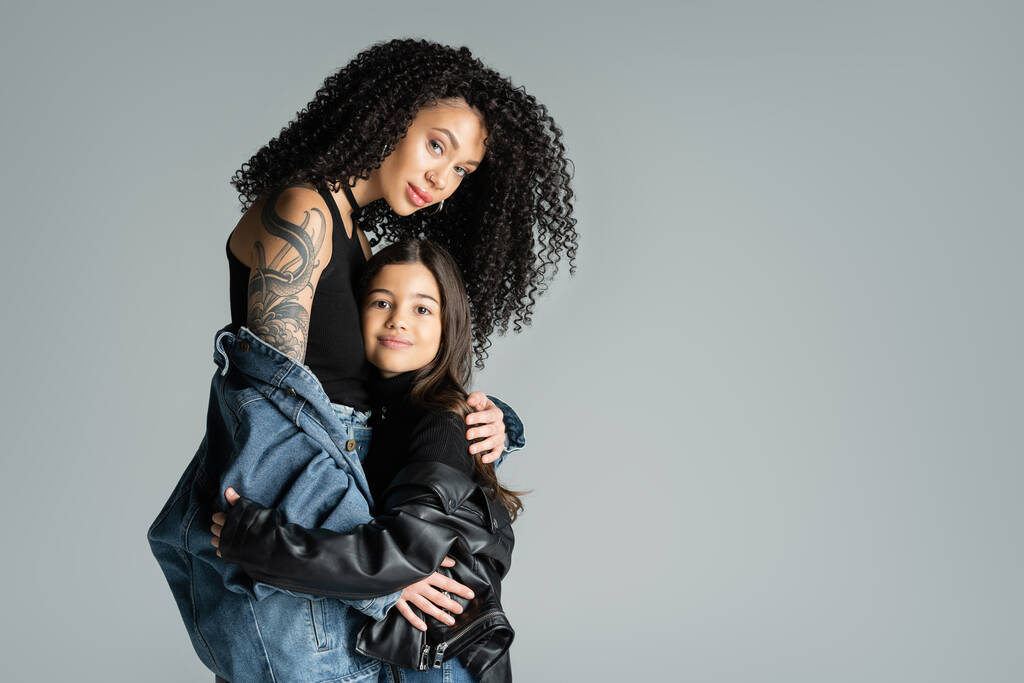Μοντέρνο και τατουάζ γυναίκα αγκαλιάζει το παιδί απομονωμένο σε γκρι  - Φωτογραφία, εικόνα
