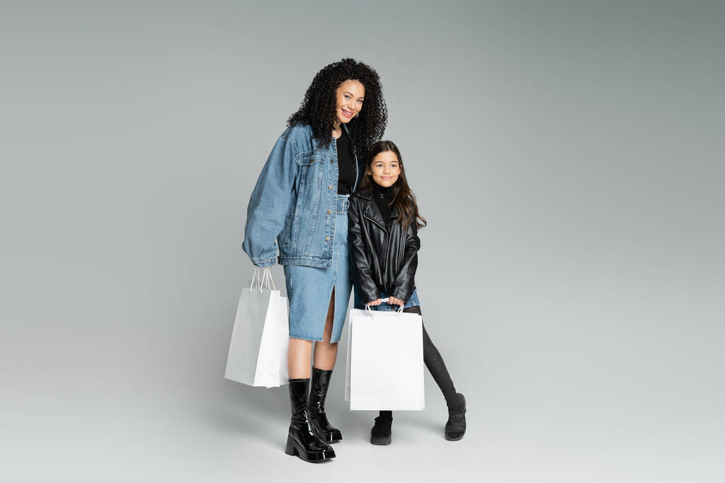 Модная мать и дитя-подросток, держащие покупки на сером фоне  - Фото, изображение