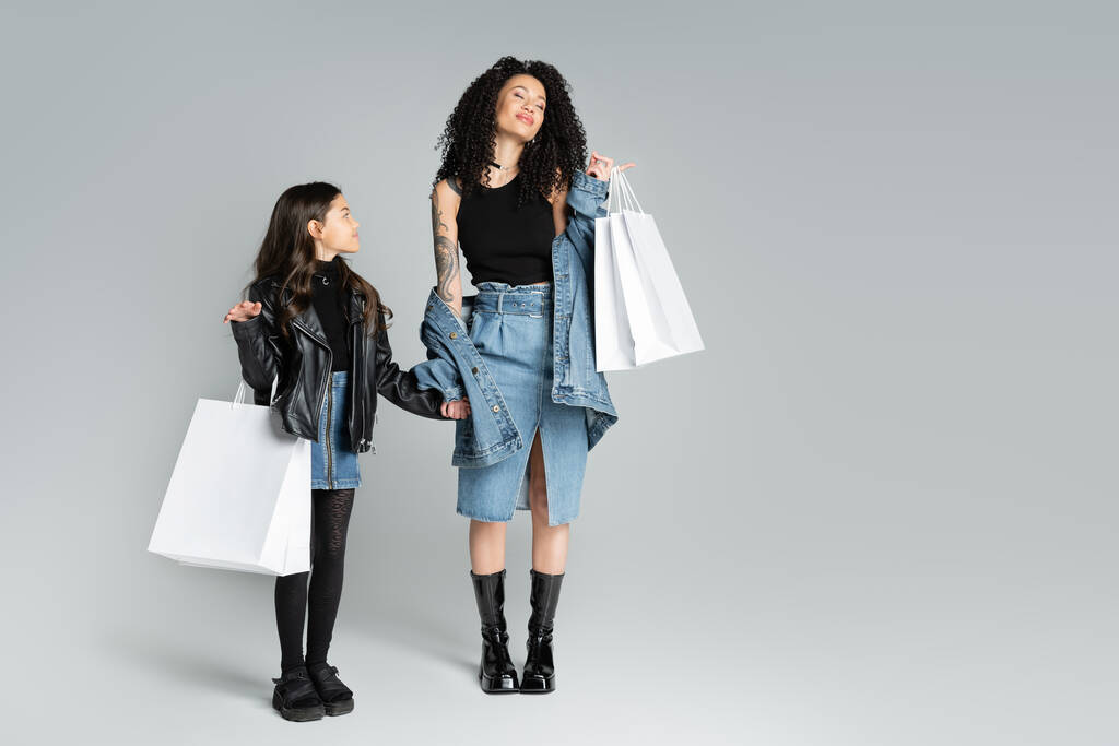 Vidám nő gazdaság bevásárló táskák és keze stílusos lánya szürke háttér  - Fotó, kép