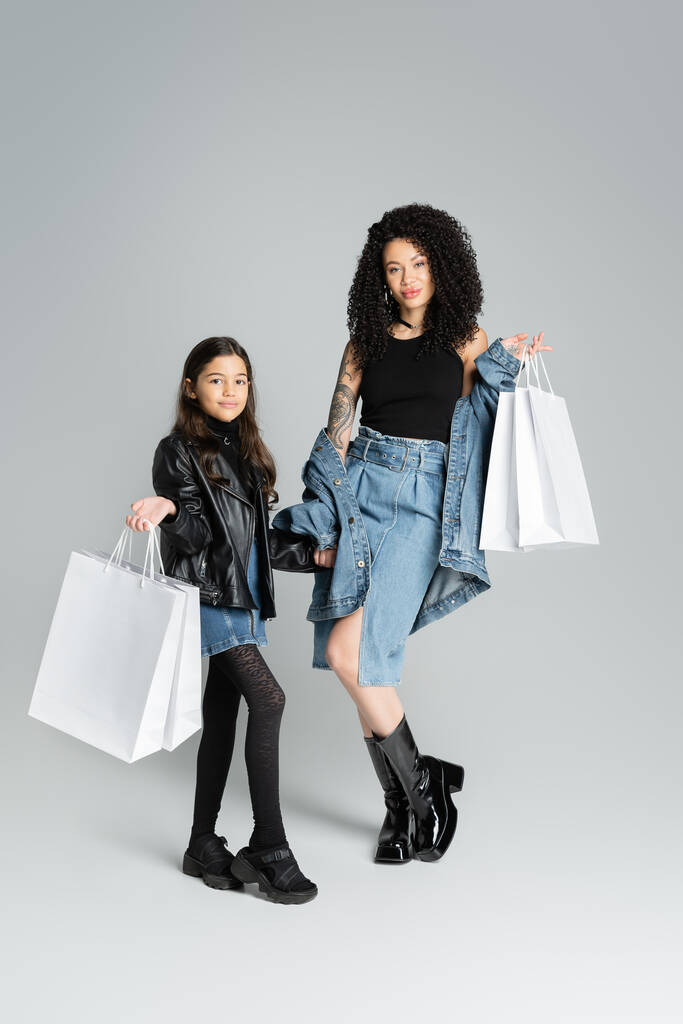 Trendy mother and daughter holding shopping bags on grey background  - Φωτογραφία, εικόνα