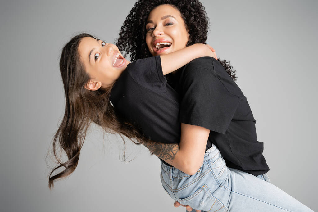 Cheerful woman hugging excited preteen daughter isolated on grey  - Zdjęcie, obraz