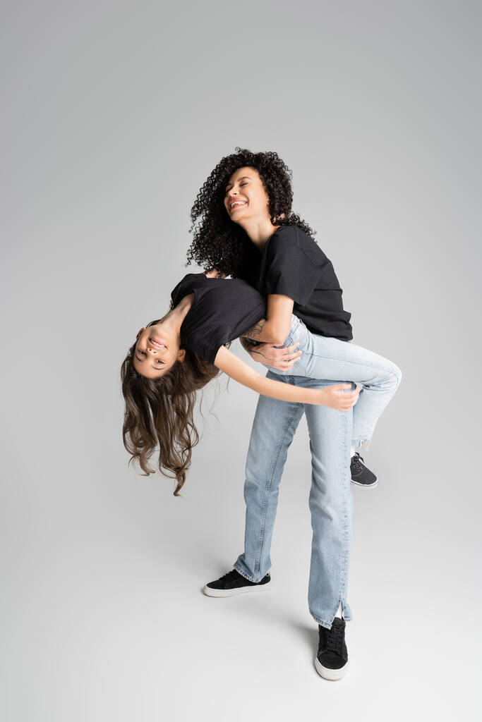 Full length of positive woman having fun with preteen kid on grey background  - Photo, Image