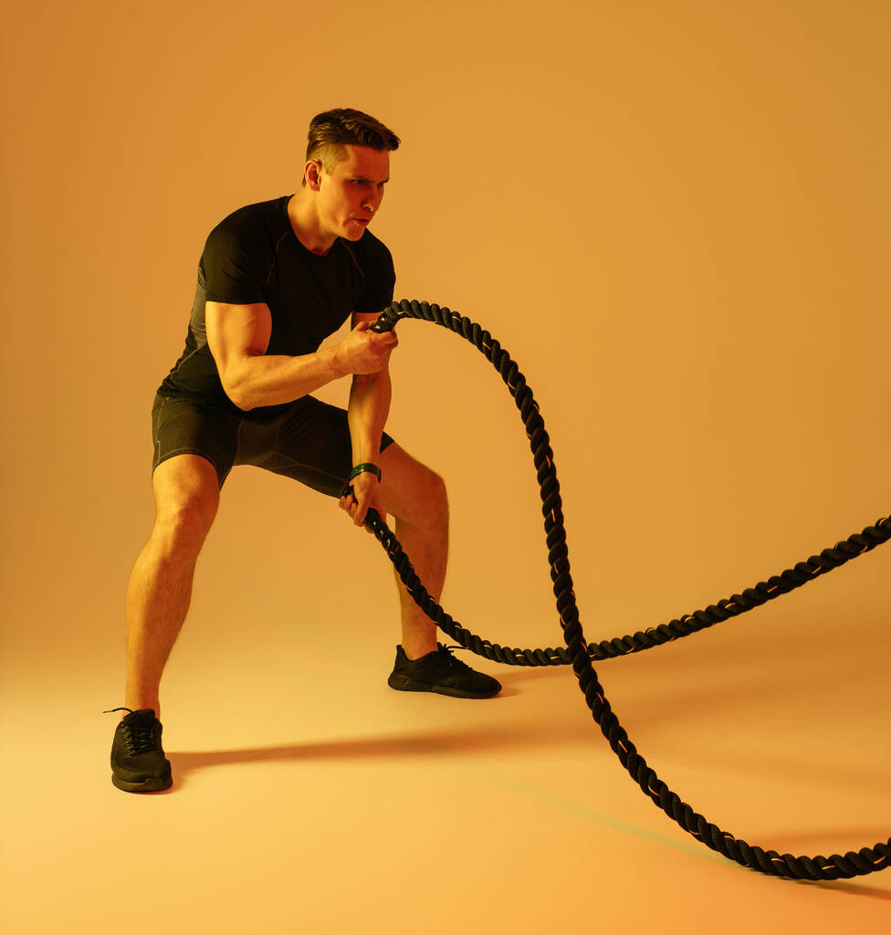 Hombre atlético con entrenamiento corporal muscular en forma en el estudio - Hombre activo haciendo un entrenamiento, iluminación colorida y fondo, conceptos sobre fitness, deporte y estilo de vida saludable - Foto, imagen