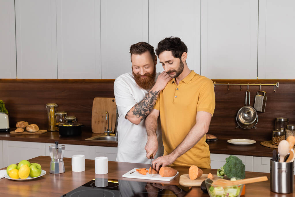 glimlachen gay man knuffelen partner koken in keuken thuis  - Foto, afbeelding