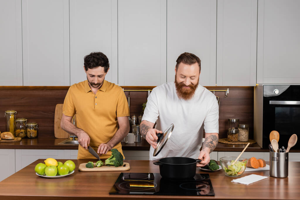 Bearded same sex couple cooking together in kitchen  - Фото, изображение