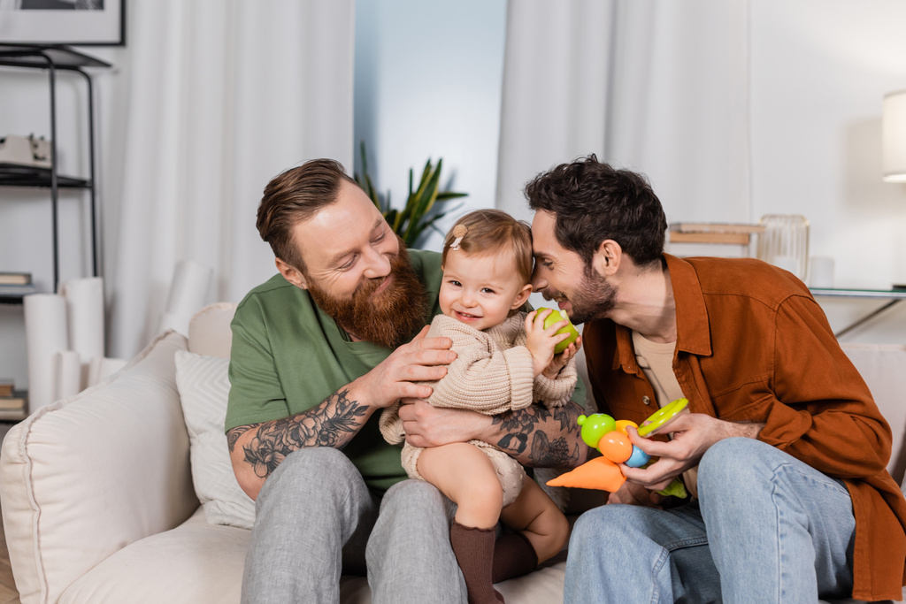 feliz gay pareja holding bebé chica con manzana en sala de estar  - Foto, imagen