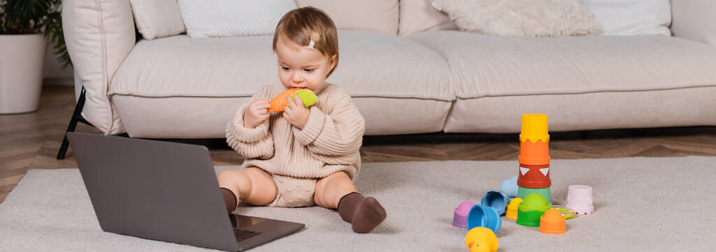 Toddler girl holding toy and looking at laptop at home, banner  - Fotografie, Obrázek