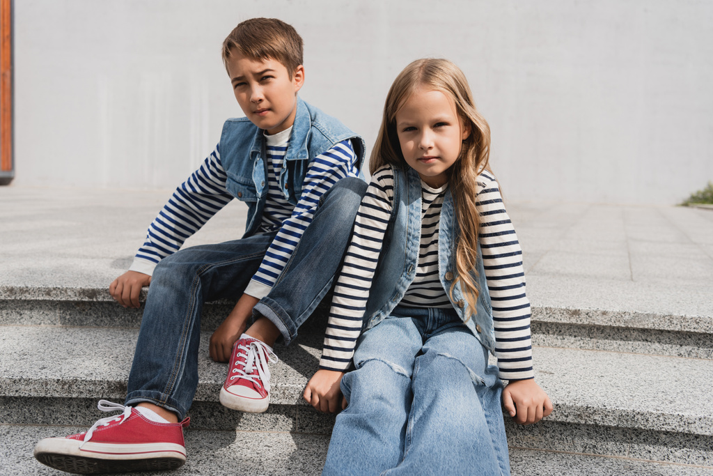 καλά ντυμένα παιδιά σε denim γιλέκα με μακρύ μανίκι πουκάμισα κάθεται στις σκάλες κοντά στο εμπορικό κέντρο  - Φωτογραφία, εικόνα