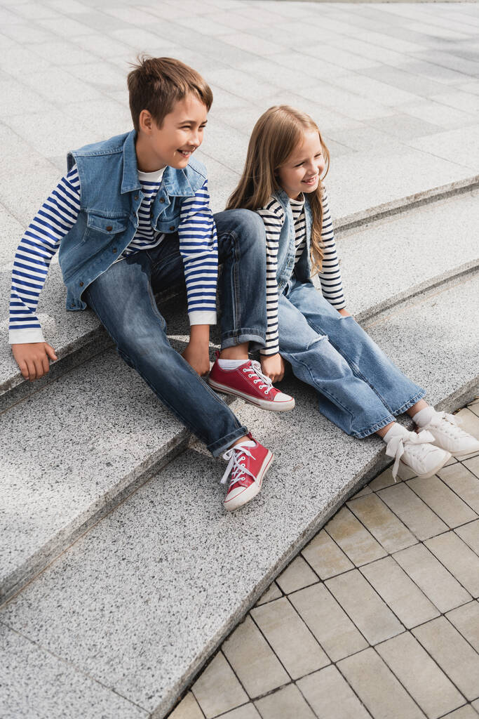 full length of cheerful well dressed children sitting on stairs of urban street  - Fotoğraf, Görsel